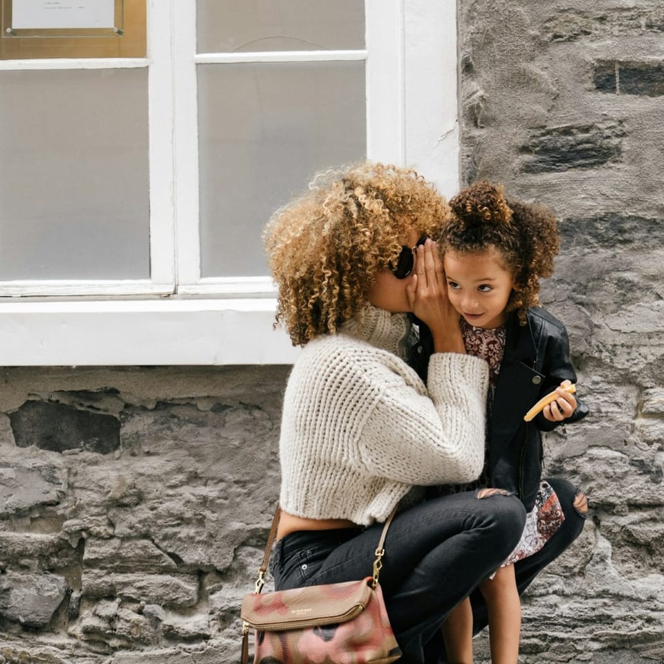 A mother whispering to her child next to a building